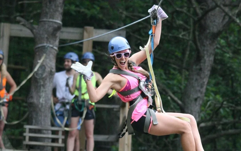 A smiling guest ziplining through the forest canopy with arms outstretched