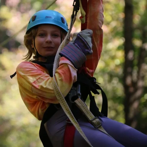 A child in a blue helmet and full harness on the zip line at Ocoee Ziplines
