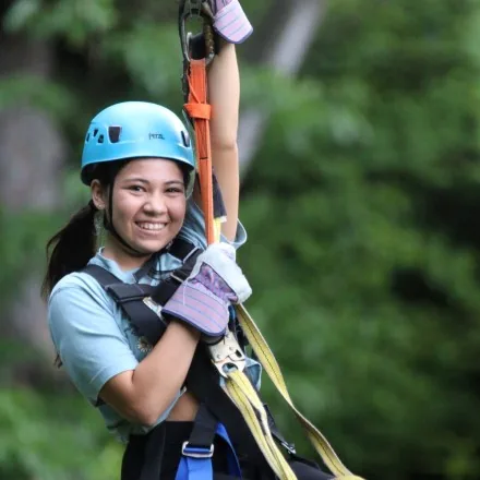 A young guest in helmet and harness riding a zip line through the trees